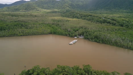 Ferry-boat-departs-in-delta-brown-water-landscape-forested-hills-Daintree-River-Aerial-drone-panoramic-view