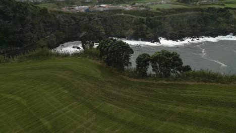 Antena-Sobre-Un-Acantilado-Con-Campo-De-Pradera-Que-Revela-La-Bahía-De-La-Isla-Volcánica,-Azores