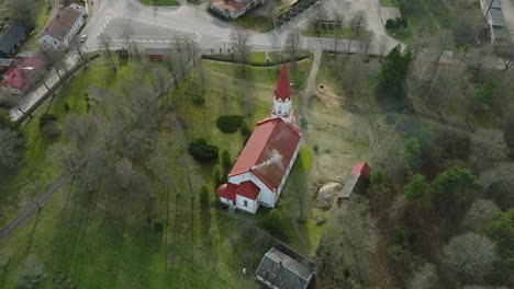 Aerial-view-of-a-white-church-with-red-roof-on-a-sunny-spring-day,-wide-angle-drone-shot-moving-forward,-tilt-down
