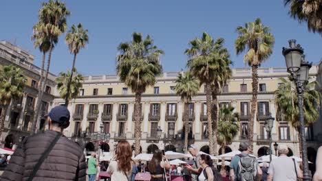 Crowded-plaza-in-Barcelona-with-tourists-and-palm-trees,-sunny-day,-handheld-shot