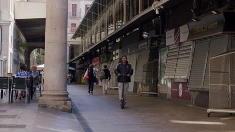 Quiet-afternoon-at-a-closed-market-in-Barcelona-with-people-strolling-by,-cafe-in-background,-ambient-mood