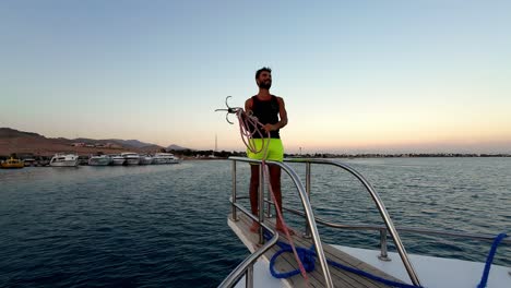 A-Man-Pulls-the-Anchor-Rope-as-They-Approach-the-Shore-of-the-Red-Sea,-Dahab,-Sinai-Peninsula,-Egypt---Medium-Shot