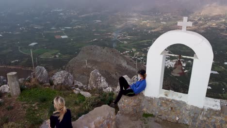 Hikers-Sit-on-Mountain-Top-and-Enjoy-Epic-360-Degree-Viewpoint-High-Above-Rocky-Cliff