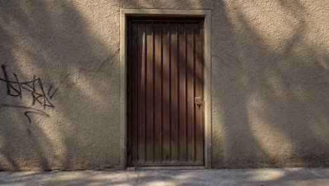 Brown-metallic-door-on-wall-with-texture-and-grafitti-at-the-afternoon,-slow-dolly-in