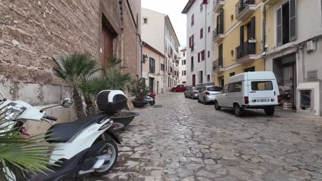 An-alley-in-Palma-De-Mallorca-with-typical-Mallorca-architecture,-cars,vintage-Renault-and-motorcycle-parked-on-the-street