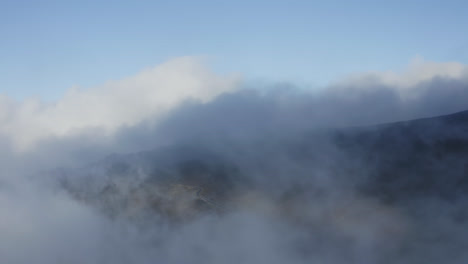 Wispy-clouds-rise-pushing-across-slopes-of-Haleakala,-aerial-overview