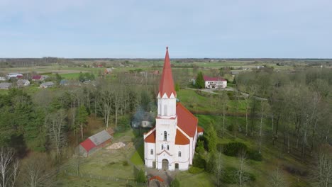 Aerial-view-of-a-white-church-with-red-roof-on-a-sunny-spring-day,-wide-angle-shot-moving-forward