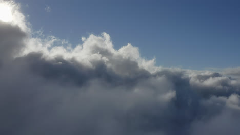 Sunlight-diffuses-light-between-thick-white-fluffy-cloudscape-texture,-aerial-dolly