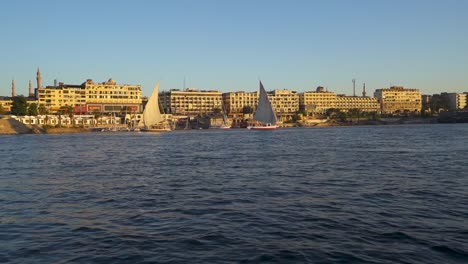 Un-Día-Soleado-En-Egipto-En-El-Río-Nilo-En-La-Ciudad-De-Asuán-Presenta-Veleros,-Riberas-Bulliciosas,-Paisajes-Urbanos-Antiguos-Y-Una-Atmósfera-Urbana-Vibrante