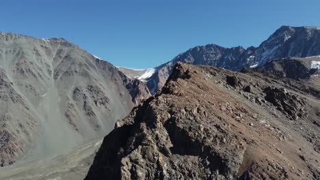 Mountain-aerial-orbits-ridge-to-reveal-snowy-alpine-cirque,-Argentina