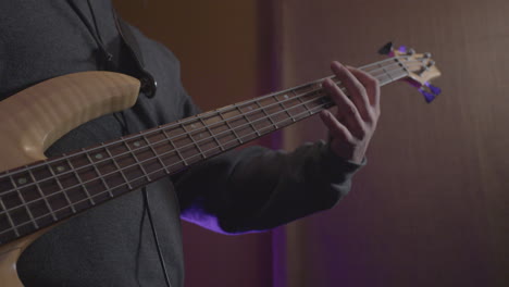 close-up-of-a-bass-guitarist-playing-a-song-on-a-bass-guitar-in-a-recording-studio-with-his-band