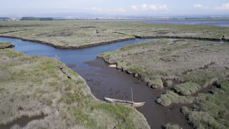 abandoned-wooden-boat-rests-in-narrow-waterway-amidst-verdant-marshlands-of-Estarreja,-Aveiro,-Portugal---aerial