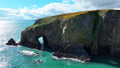 Drone-reveal-from-sea-cave-and-cliffs-to-view-of-coastline-emerald-sea-and-mountain-with-dramatic-clouds-in-background-in-Waterford-Ireland