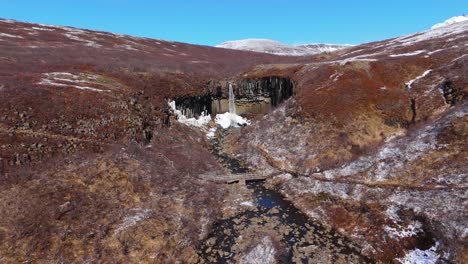 Skyline-Berghintergrund-In-Isländischen-Svartifoss-Wasserfällen,-Luftdrohne-Zoomt-In-Kaskadierendes-Wasser,-Schwarze-Versteckte-Nationalparklandschaft