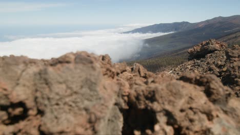 From-behind-the-rock-there-is-a-view-of-the-mountains-covered-in-clouds,-Tenerife-park-in-Spain