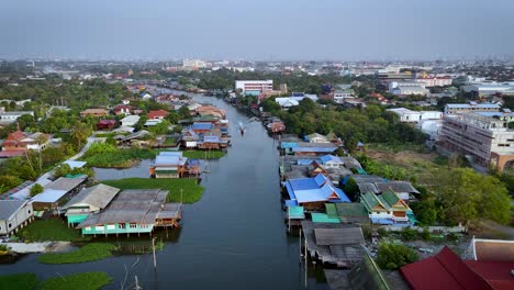 Eine-Drohnenaufnahme-Eines-Longtail-Bootes,-Das-über-Einen-Wasserweg-In-Einem-Vorort-Außerhalb-Von-Pak-Kret,-Thailand-Gleitet