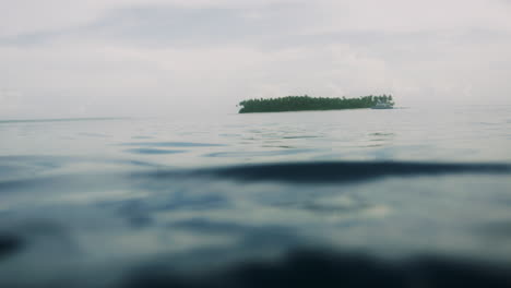 Placid-calm-ocean-water-with-small-island-off-in-distance,-low-angle