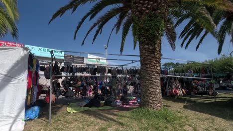 African-immigrant-sells-counterfeit-women's-handbags-to-tourists-in-his-street-shop-under-palm-trees-one-summer-morning,-shooting-traveling-backwards