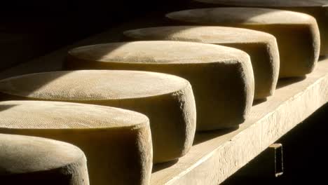 cheese-wheels-on-wooden-shelf-in-mountain-pasture-hut,-natural-sunlight,-zoom-in