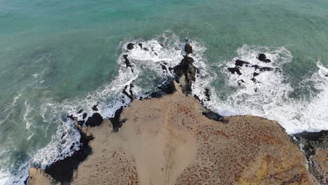 Acantilados-Aéreos-De-Arena-Oceánica-De-Arriba-Hacia-Abajo-En-Una-Playa-De-Espuma-Blanca,-Olas-Azules-Aplastan-La-Costa