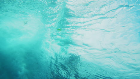 Underwater-rearview-of-surfer-catching-steep-wave-into-barrel