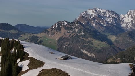 Vista-Aérea-De-Las-Casas-Casi-Medio-Enterradas-En-La-Nieve-En-La-Estación-De-Esquí-De-Amden,-Con-La-Gigante-E-Imponente-Montaña-Säntis-Al-Fondo