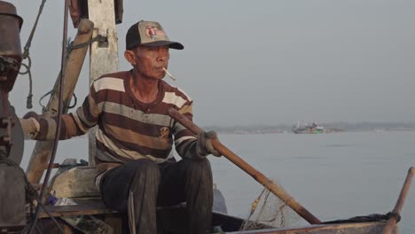 An-elderly-fisherman-enjoys-a-cigarette-while-skillfully-casting-fishing-nets-using-bamboo,-a-technique-passed-down-through-generations