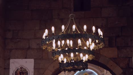 Medieval-style-chandelier-with-lit-candles-in-an-old-stone-chamber