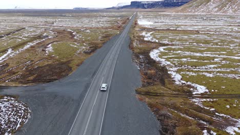 Aerial-Drone-Follows-White-Car,-Drive-through-Icelandic-Volcanic-Snowy-Mountains