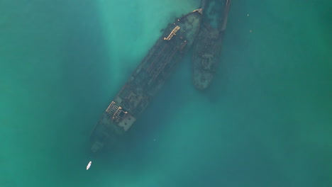 Slow-Aerial-Top-Down-Rusty-remains-of-shipwreck,-old-ship-sunk-in-the-blue-sea