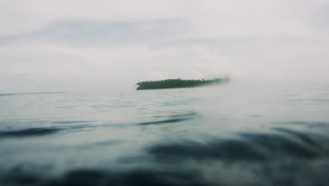 Pequeña-Isla-Tropical-De-Atolón-En-La-Distancia-Detrás-De-La-Tranquila-Superficie-Del-Agua-Del-Océano