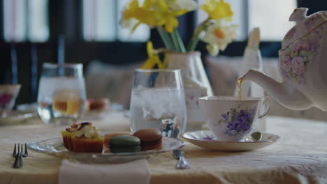 Elegante-Mesa-De-Té-Con-Hermosas-Flores-Amarillas,-Pasteles-Coloridos-Y-Utensilios-De-Té-Antiguos