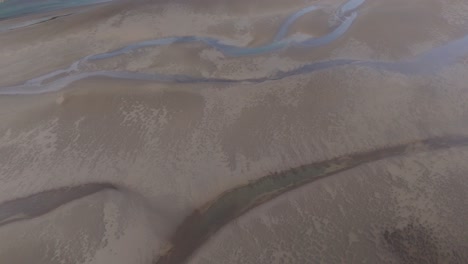 Aerial-drone-fly-rivers-through-sand-black-glacial-Icelandic-soil-textured-earth