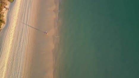 Vertical-Drone-Follows-White-sand-beach-path,-sea-water-coastline,-couple-walks-along-shore,-aerial-tops-down