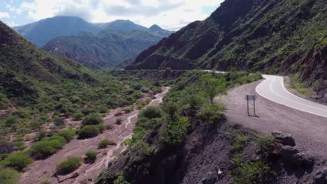 Mountain-aerial-follows-highway-along-dry-river-bed,-Argentina-nature