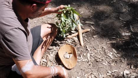 Australian-Aboriginal-Smoking-Ceremony,-man-creates-smoke-on-a-traditional-wooden-bowl-as-part-of-an-ancient-indigenous-custom