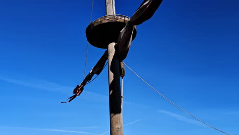 Wooden-ship-mast-sailing-vessel-clear-blue-sky-flagpole-spar-sail