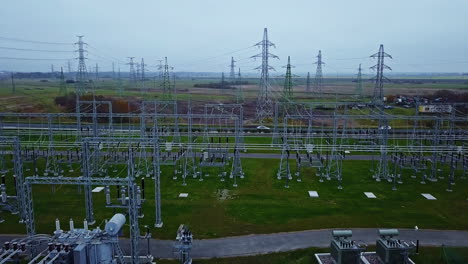Drone-rising-in-front-of-a-electrical-transmission-substation,-dark,-cloudy-day