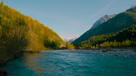 Gebirgsfluss-Mit-Klarem,-Blauem-Wasser,-Der-An-Leuchtend-Bunten-Herbstbäumen-In-Der-Sonne-Vorbeirauscht