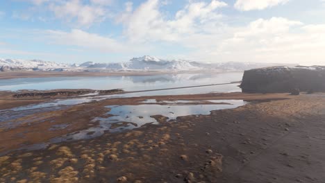 Vulkanische-Bodenbildung-Rund-Um-Schneebedeckte-Berge,-Isländischer-See,-Drohne,-Sonniger-Tag