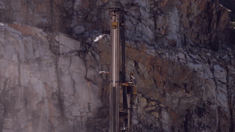 Vertical-drilling-rig-piercing-through-the-rock-face-of-a-stark-quarry-cliff