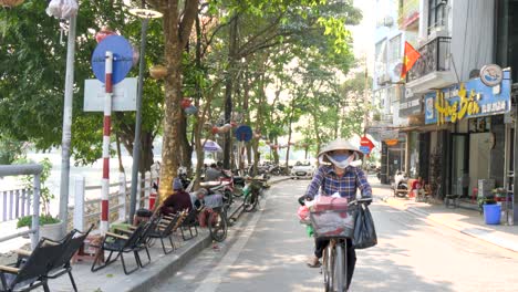 Sunny-day,-downtown-Hanoi-city,-masked-residents-travelling-on-cycles