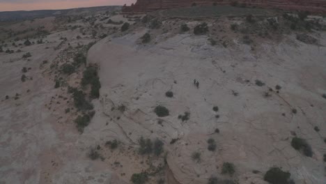 Luftaufnahme-Von-Zwei-Personen,-Die-Bei-Sonnenuntergang-Mit-Ihren-Mountainbikes-Auf-Slickrock-Durch-Die-Riesigen-Canyons-Der-Moab-Wüste-Fahren