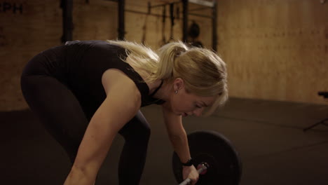 Strong-blonde-woman-in-black-does-snatch-weightlifting-move,-cinematic-lighting