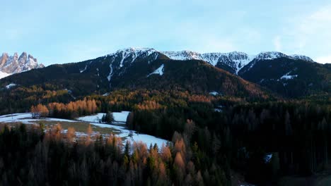Vista-De-Drones-De-Un-Bosque-En-Las-Montañas-Dolomitas-En-Italia-Al-Atardecer-Con-Sol,-Nieve,-Picos,-Paisaje,-Reflejos-De-Luz-Y-Cielo-Azul