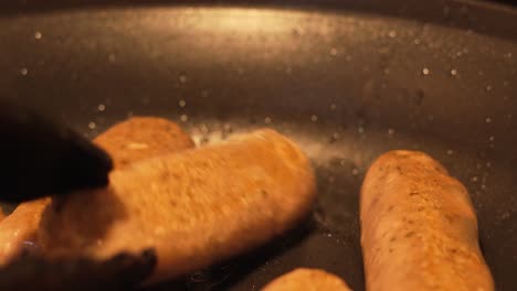 Close-Up-of-Chef-Using-Tongs-to-Turn-Sausages-in-Hot-Frying-Pan