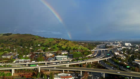 Toma-De-ángulo-Alto-Sobre-El-Paso-Elevado-De-La-Autopista-En-La-Ciudad-De-Walnut-Creek-En-El-Condado-De-Contra-Costa,-California,-Estados-Unidos,-Con-Un-Arco-Iris-Visible-En-El-Fondo