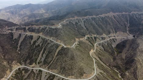 rotating-aerial-view:-scenic-road-switchbacks-down-mountain-slope