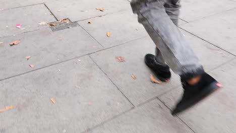 Paseo-Urbano-En-Londres,-Hombre-Con-Zapatillas-Negras,-Pantalones-Grises-Caminando-Lentamente-Entre-Hojas-De-Otoño