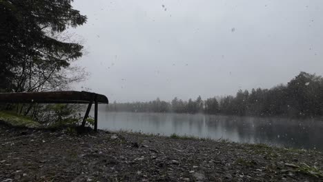 Grandes-Copos-De-Nieve-Caen-Sobre-Un-Banco-Con-Vistas-Al-Lago-Místico-En-Primavera